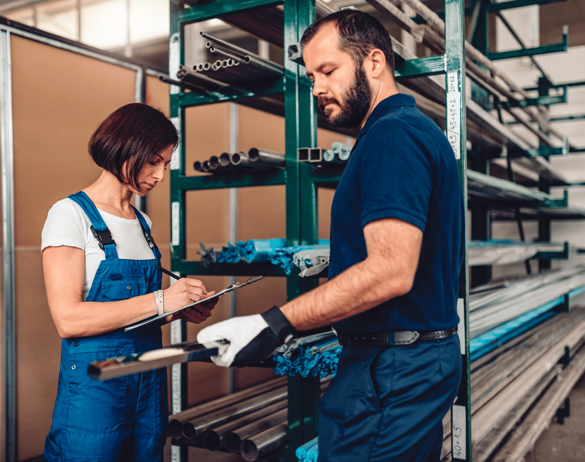 Mann und Frau stehen vor einem Regal mit Metallteilen und bearbeiten gemeinsam einen Auftrag.